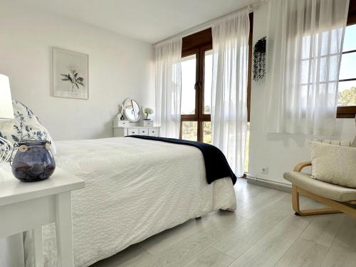 a white bedroom with a large bed and a chair at "LAS CAMELIAS SOMO" un lugar para desconectar!! Vistas al MAR!! in Somo