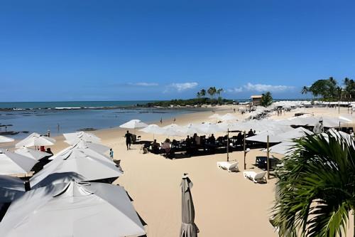 a beach with white umbrellas and people on the beach at MAR DÁ LIBERDADE com Villa das Ondas in Morro de São Paulo