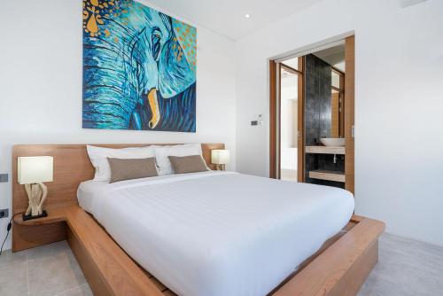 a bedroom with a large white bed and a painting at Eden Escape Naiyang Beach in Phuket Town