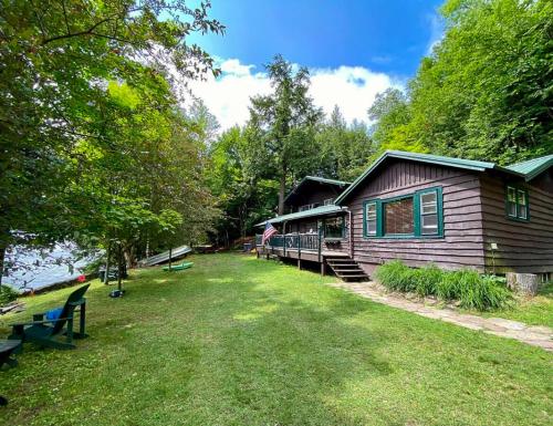 Una cabaña con un patio de césped al lado de un edificio. en Lakefront Adirondack Cabin - Dock - Canoe - 10 min to Lake Placid, en Saranac Lake