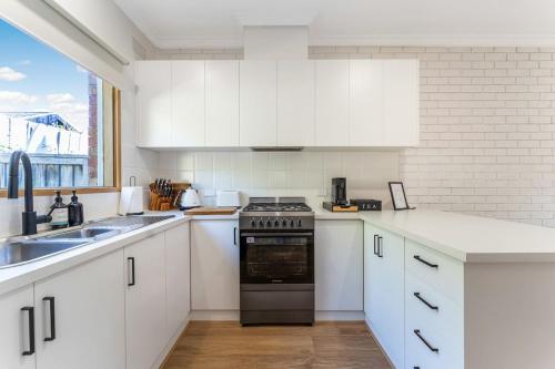 a white kitchen with a stove and a sink at Cozy Newtown 2 bedroom unit in Geelong
