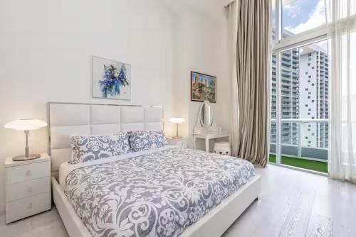 a white bedroom with a bed and a large window at Beautiful Icon Brickell Double height ceiling in Miami