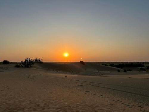 a sunset in the desert with the sun setting in the horizon at HAMIRGARH LUXURIOUS DESERT CAMP & RESoRT in Jaisalmer