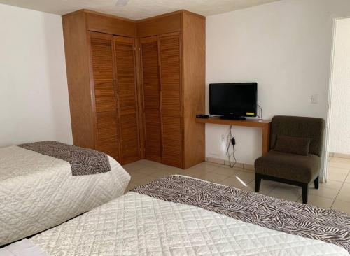a bedroom with two beds and a chair and a television at Agradable y amplio depa cerca del metropolitano in Guadalajara