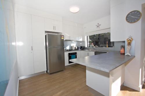 a kitchen with white cabinets and a stainless steel refrigerator at Beach Stayz Semaphore Three Bedroom Apartment in Port Adelaide