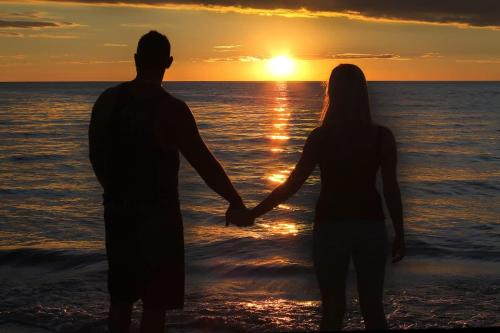 a man and woman standing on the beach watching the sunset at Beach Stayz Semaphore Three Bedroom Apartment in Port Adelaide