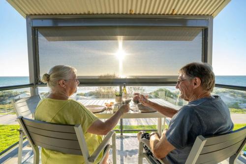 two older people sitting at a table with a view of the ocean at Beach Stayz Semaphore Upstairs Two Bedroom Apartment in Port Adelaide