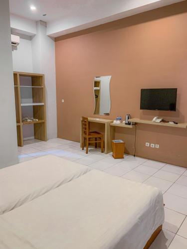 a bedroom with a bed and a desk and a television at Prima SR Hotel & Convention Yogyakarta in Yogyakarta