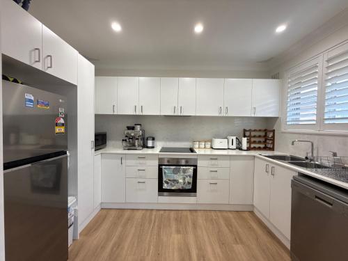 a kitchen with white cabinets and a stove top oven at Coogee Sunrise 2 Bed Apt with Parking, Work Desks & Balcony in Sydney