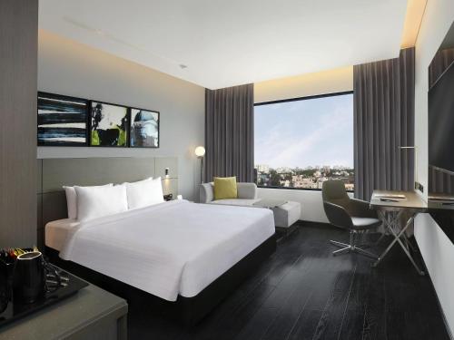 a hotel room with a large white bed and a desk at Novotel Chennai Chamiers Road in Chennai