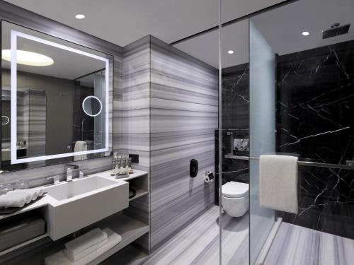 a bathroom with a sink and a toilet and a mirror at Novotel Chennai Chamiers Road in Chennai