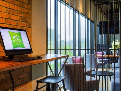 a computer sitting on a desk in a room with windows at ibis Styles Kota Kinabalu Inanam in Kota Kinabalu