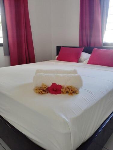 a white bed with red pillows and flowers on it at Roche Kerlan Apartments in Anse Kerlan