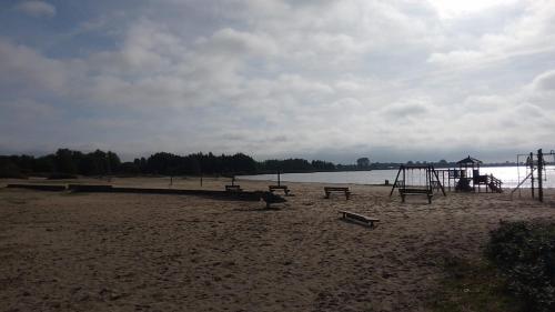 an empty playground on a beach with the water at Chalet Meerwijck mit Terrasse am Wasser und Meer mit Schwimmbad in Kropswolde