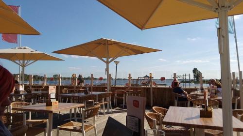 a restaurant with tables and chairs and umbrellas at Chalet Meerwijck mit Terrasse am Wasser und Meer mit Schwimmbad in Kropswolde