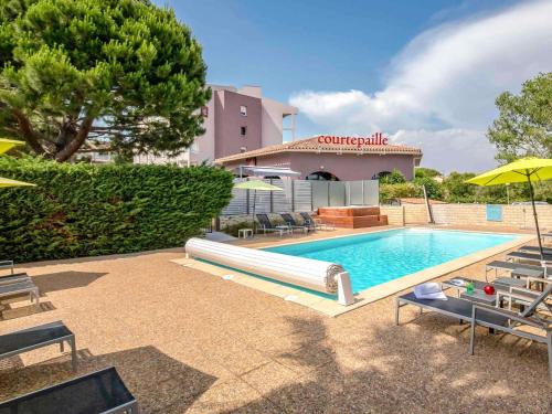 a swimming pool with chairs and umbrellas in front of a building at ibis Styles Fréjus St Raphael in Fréjus