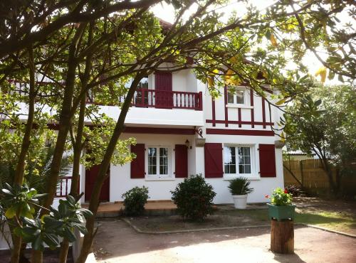 a white house with red shutters and trees at Chambre d'hôtes d'Émilie in Boucau