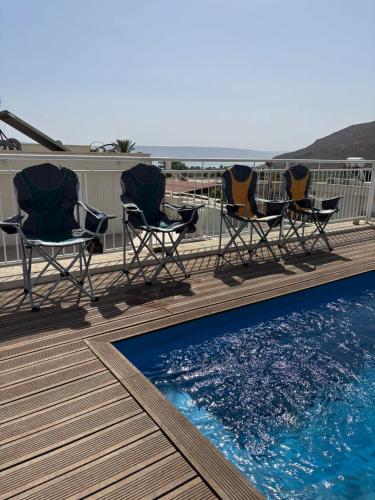 three chairs and a swimming pool on a deck at תכלת במושבה in Migdal