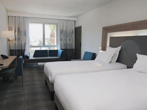 a hotel room with two beds and a desk at Novotel Mohammedia in Mohammedia