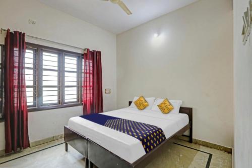 a bedroom with a bed and a window with red curtains at Hotel O Vishu Moni Residency in Mysore