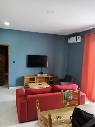 un salon avec un canapé rouge et une télévision à écran plat dans l'établissement Elysée, à Mbour