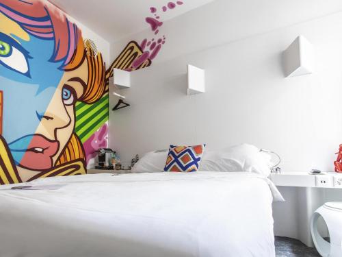 a bedroom with a white bed with a painting on the wall at ibis Styles Lausanne Center MadHouse in Lausanne