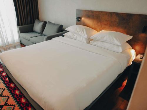 a large white bed in a room with a couch at ibis Styles Sarajevo in Sarajevo