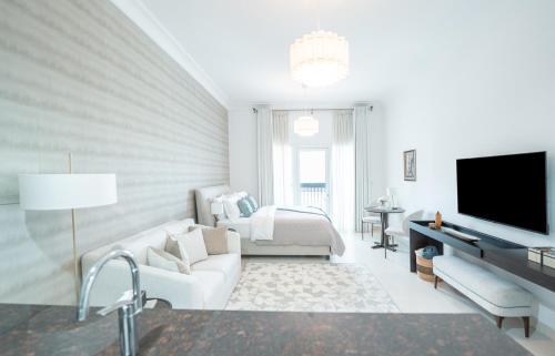 a white living room with a couch and a tv at Modern Studio Living by Voyage in Abu Dhabi