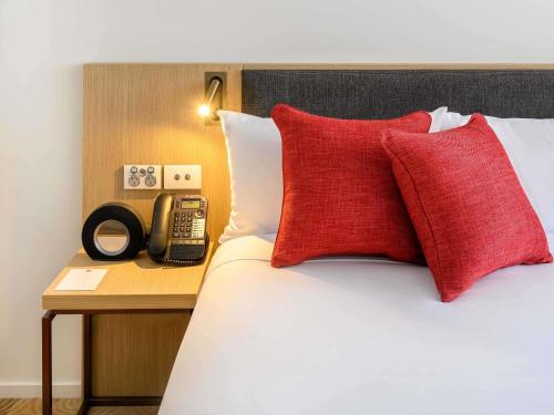 a bed with red pillows and a phone on a table at ibis Melbourne Central in Melbourne