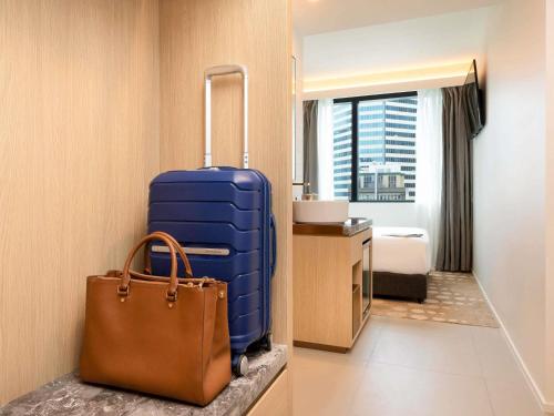 a hotel room with a blue suitcase and a purse at ibis Melbourne Central in Melbourne