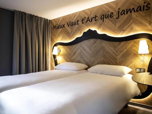 two beds in a hotel room with a sign on the wall at ibis Styles Douai Gare Gayant Expo in Douai