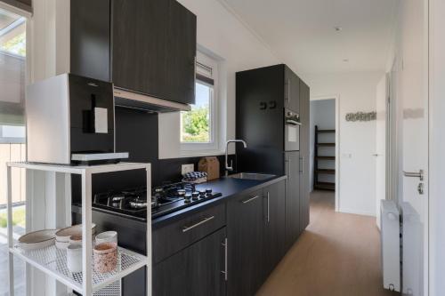 a kitchen with black cabinets and a stove at Lodges van Rongen in Heinkensand