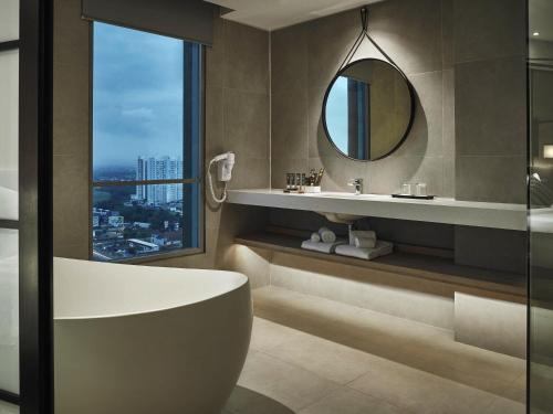 a bathroom with a tub and a mirror at Novotel Karawang in Karawang