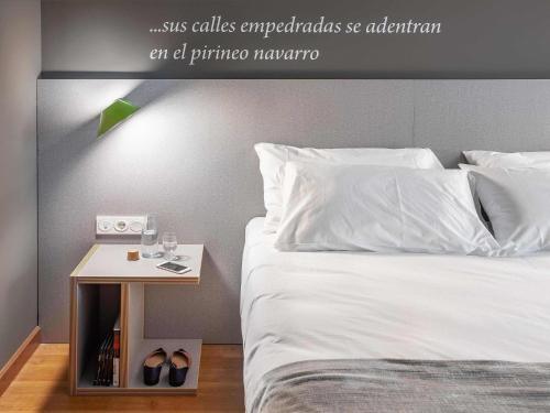 a bed with a nightstand next to a bed with white sheets at ibis Styles Pamplona Noain in Noáin