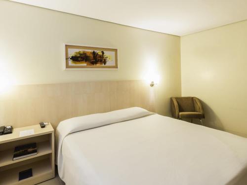 a hotel room with a white bed and a chair at ibis Styles Belem Batista Campos in Belém