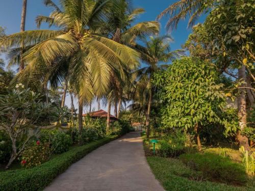 a path leading to a resort with palm trees at Mercure Goa Devaaya Resort in Old Goa