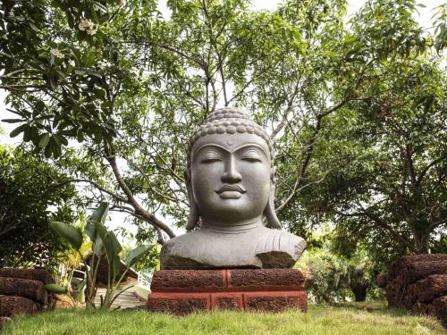 a statue sitting in the grass in front of trees at Mercure Goa Devaaya Resort in Old Goa