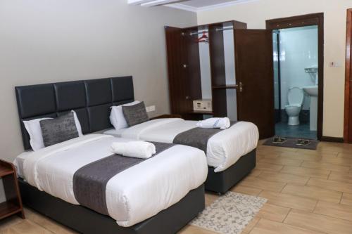 two beds in a hotel room with a bathroom at Lake Naivasha Lazarus Lodge in Naivasha