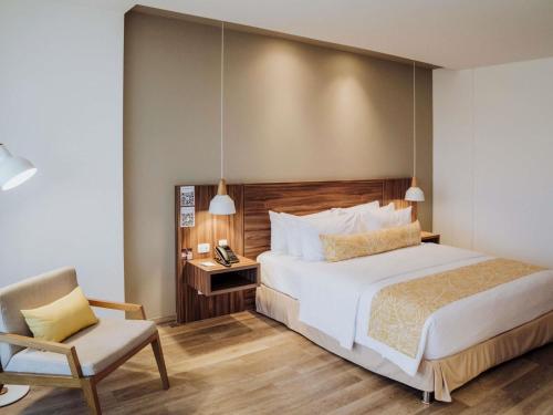 a bedroom with a large bed and a chair at Novotel Medellin El Tesoro in Medellín