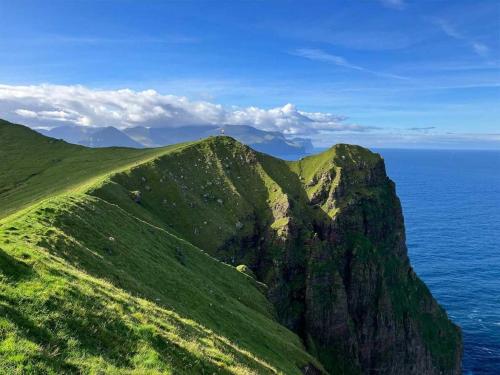 a green mountain with the ocean in the background at Modern Apartment with Balcony & Stunning Views in Argir