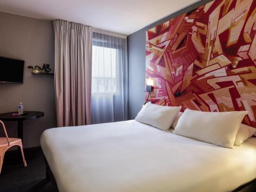 a hotel room with a large white bed with a painting on the wall at Ibis Styles Toulouse Centre Canal du Midi in Toulouse