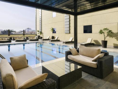 a swimming pool with couches and chairs next to a building at Ibis Jeddah Malik Road in Jeddah