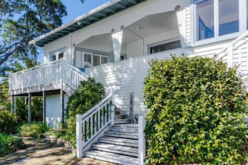 a white house with stairs in front of it at Harbour Rose House in Raglan