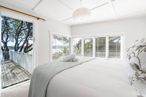 a white bedroom with a bed and large windows at Harbour Rose House in Raglan