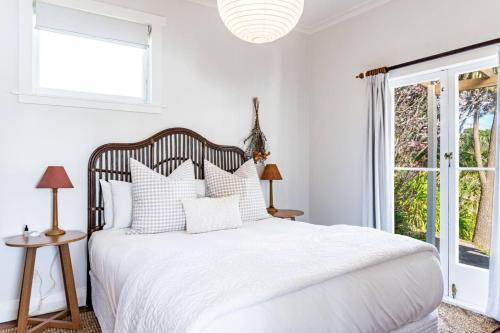 a white bedroom with a bed with white sheets and pillows at Harbour Rose House in Raglan