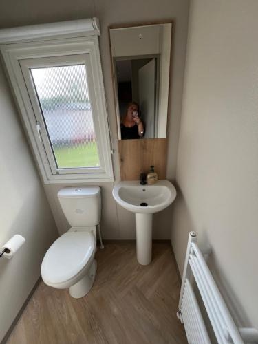 a woman taking a picture of a bathroom with a toilet and sink at The Orchards modern caravan in Saint Osyth