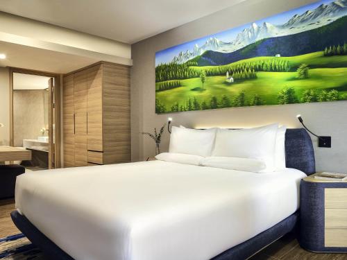 a bedroom with a white bed and a painting on the wall at Novotel Hanoi Thai Ha in Hanoi