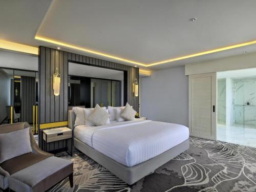 a bedroom with a large white bed and a chair at Movenpick Surabaya City in Surabaya