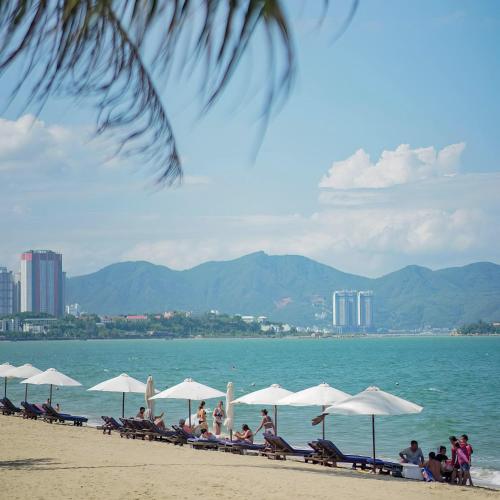 a group of people sitting on a beach with umbrellas at VELA OCEAN LUXURY SUITES Nha Trang Centre in Nha Trang