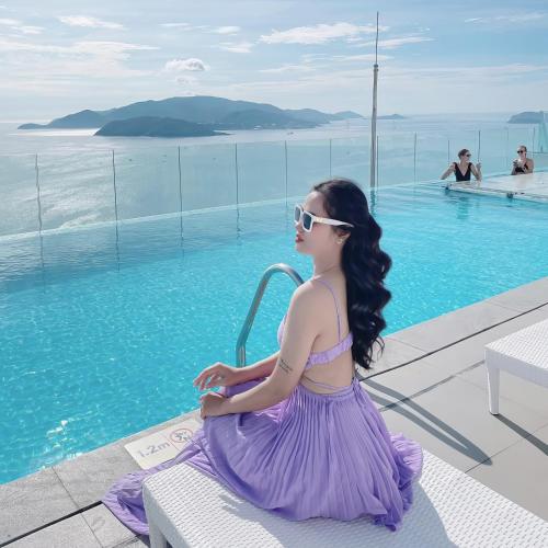 a woman in a purple dress sitting next to a swimming pool at VELA OCEAN LUXURY SUITES Nha Trang Centre in Nha Trang